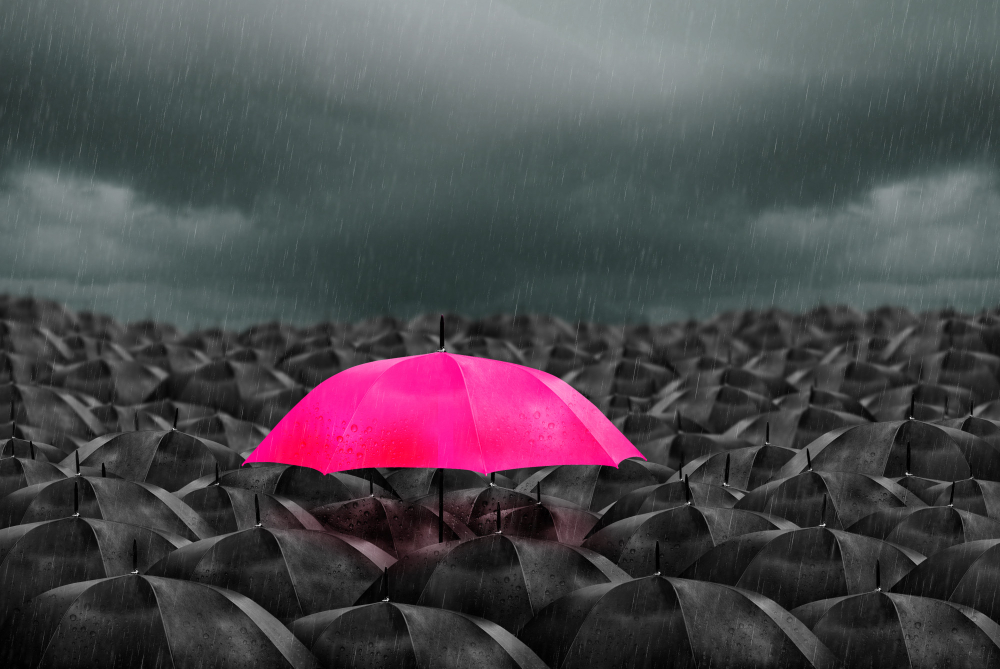 colorful pink umbrella in a sea of mass black umbrellas